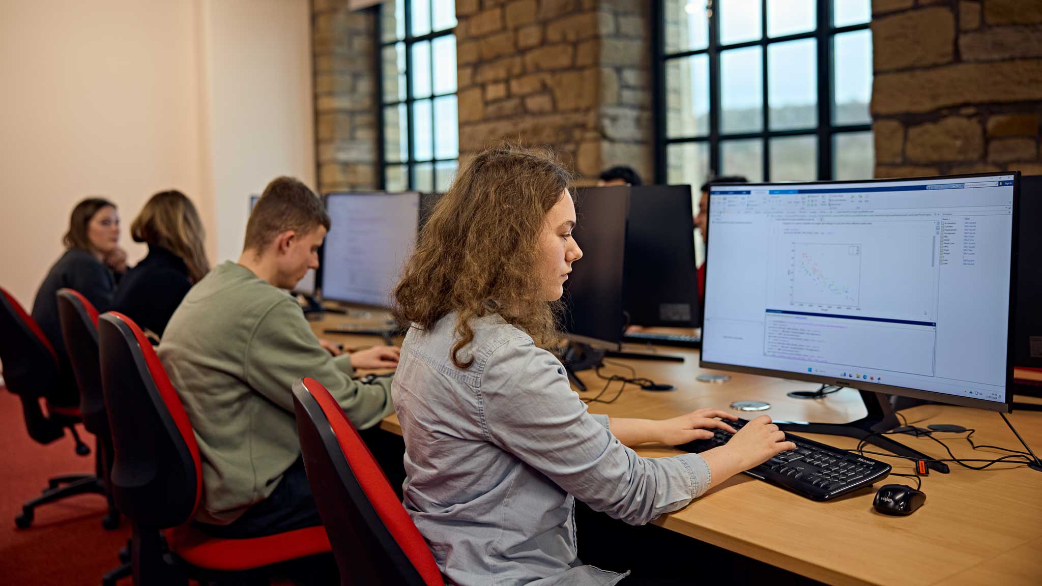 Three students working in a computer room looking at their computers