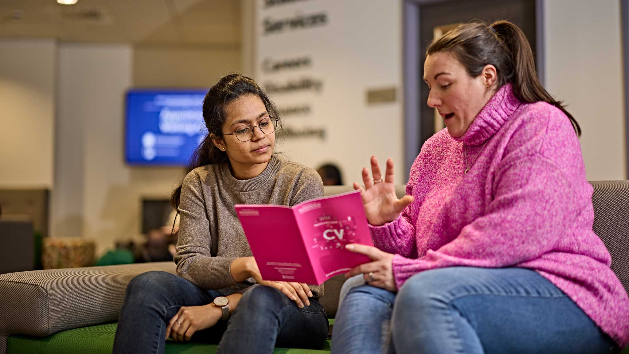 A student talking to a member of staff reading a book about CVs