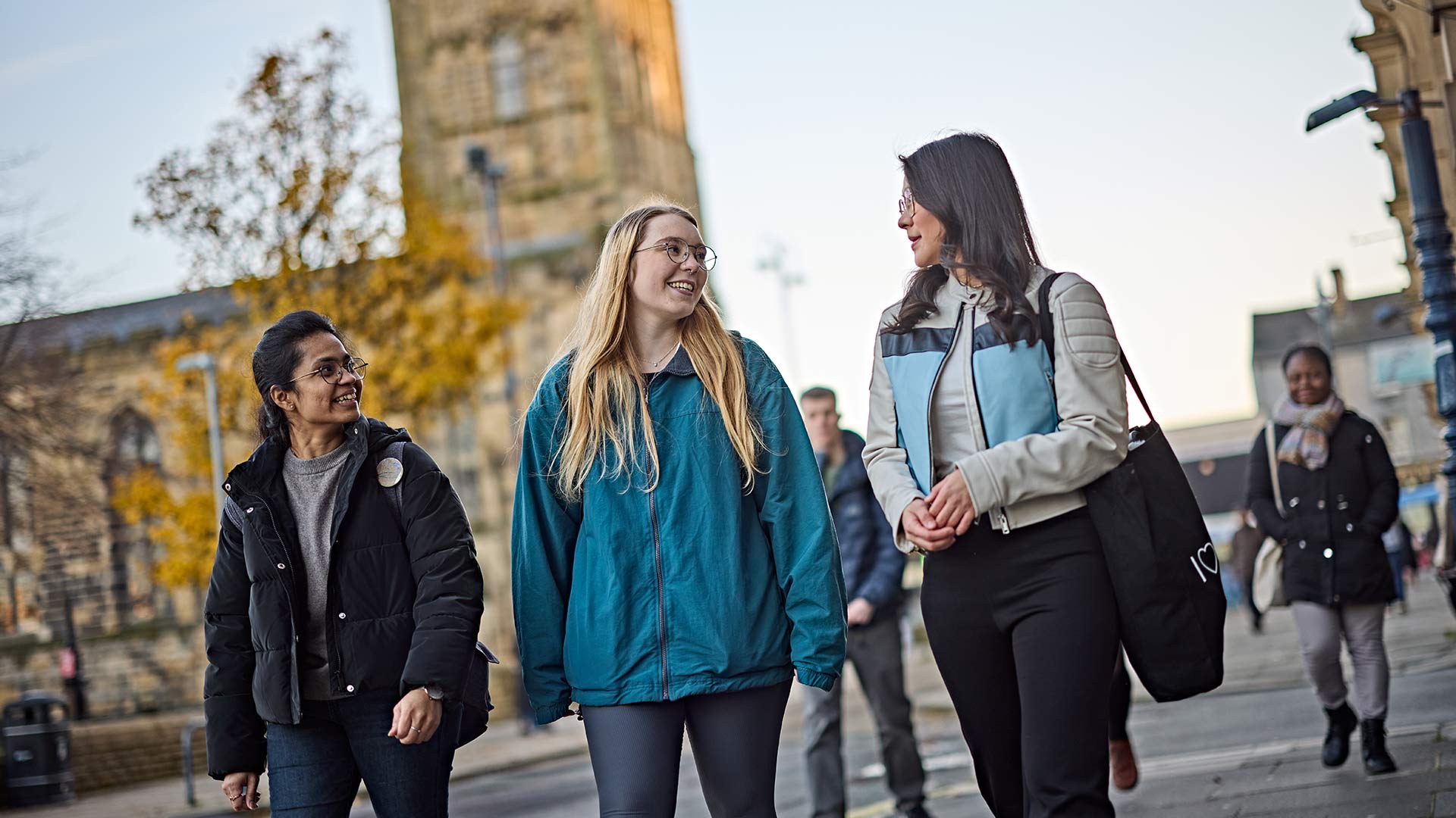 A group of students walking through Huddersfield town centre, with St Peter's Parish Church in the background.