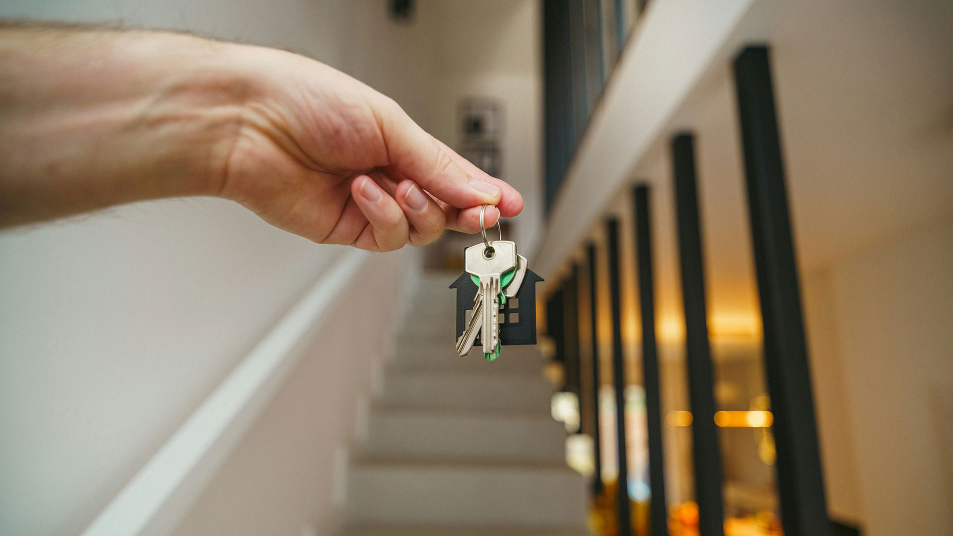 A hand holding a set of keys, with stairs in the background.