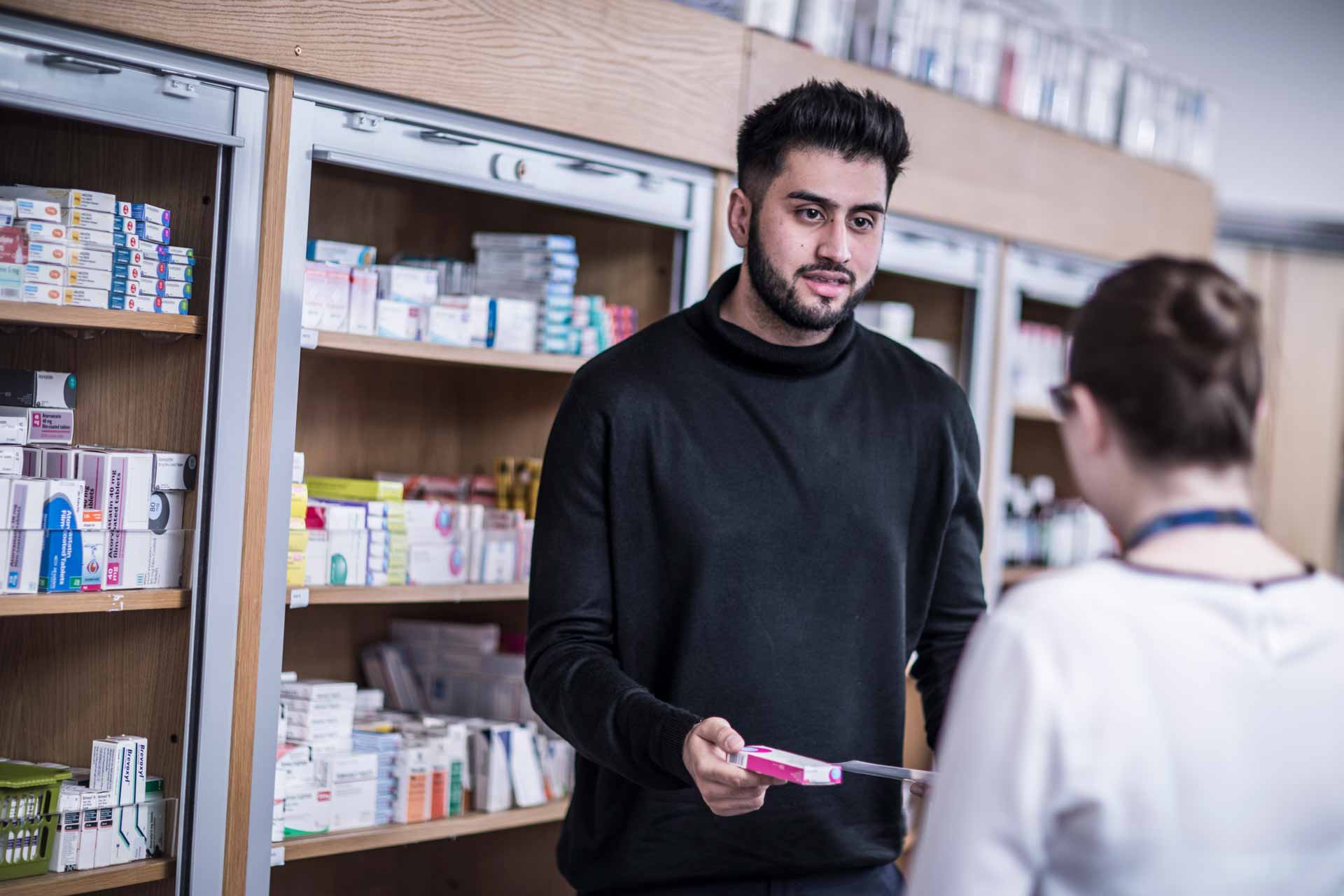 A picture of a pharmacy student handing someone a prescription. 