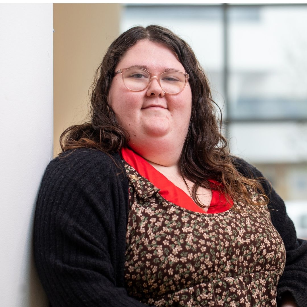 A student leaning against a wall smiling