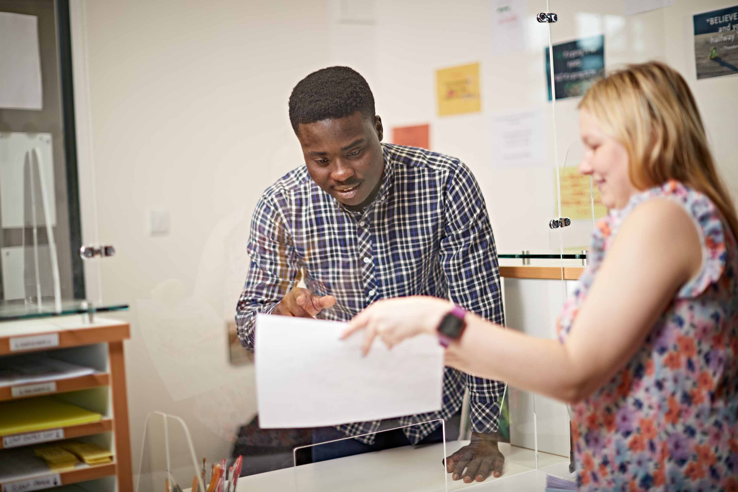 A student with a check shirt looks at a piece of paper in the student support office
