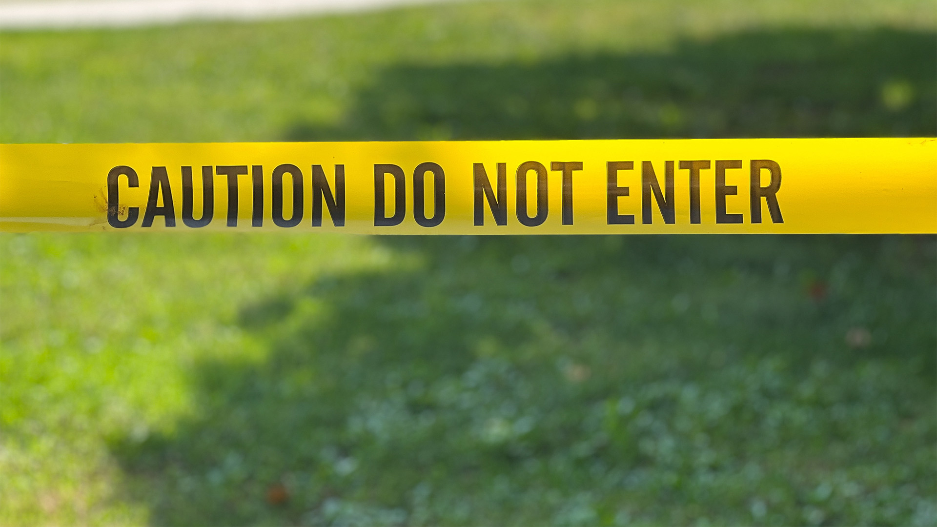 yellow caution do not enter tape across a grassy background