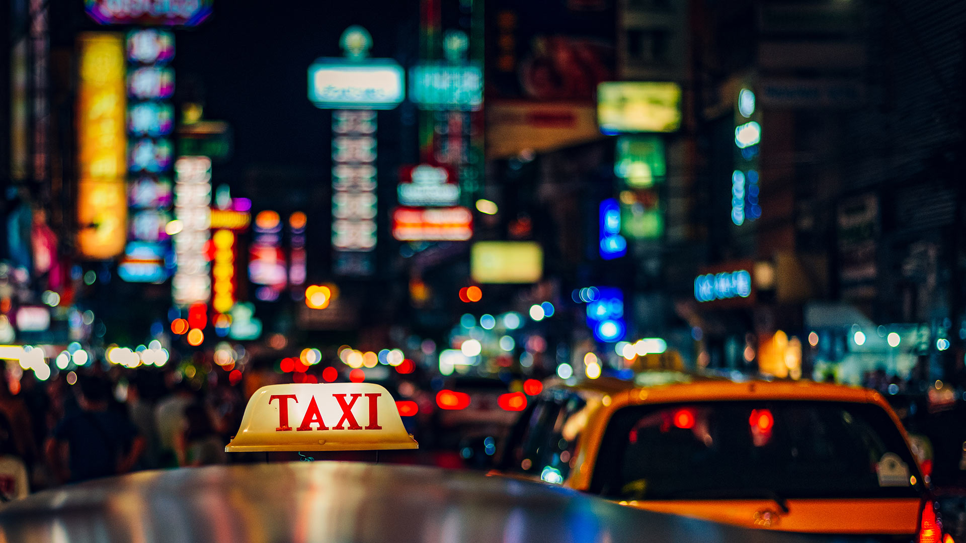 a street scene in Thailand at night with neon lights and taxis in foreground