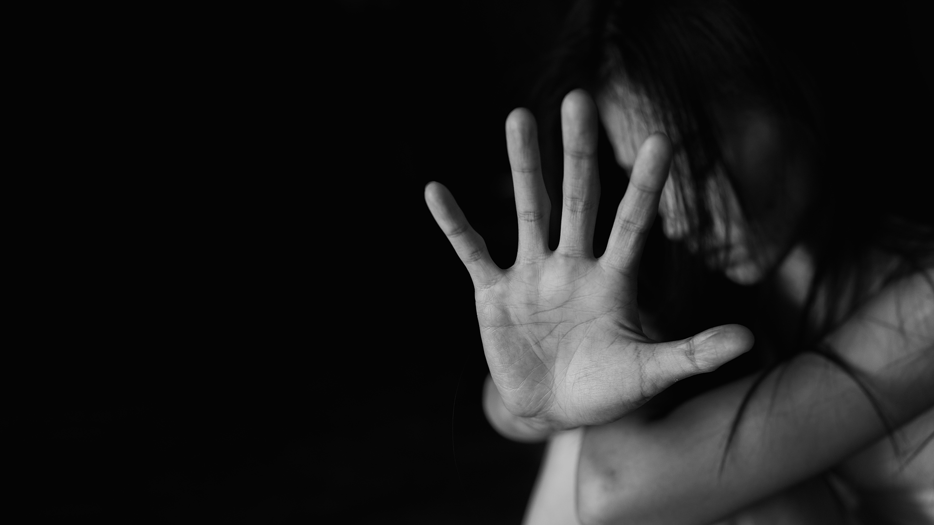 a young victim sat with the arms around their knees and a hand up to signify stop