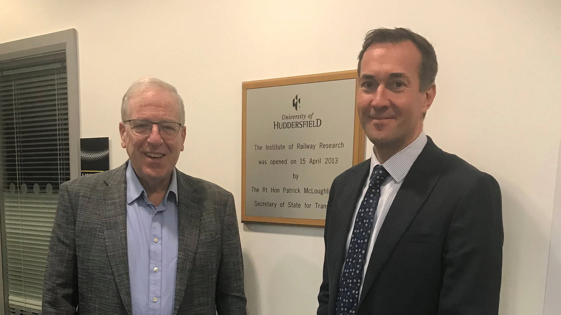 Two men standing in front of a naming plaque