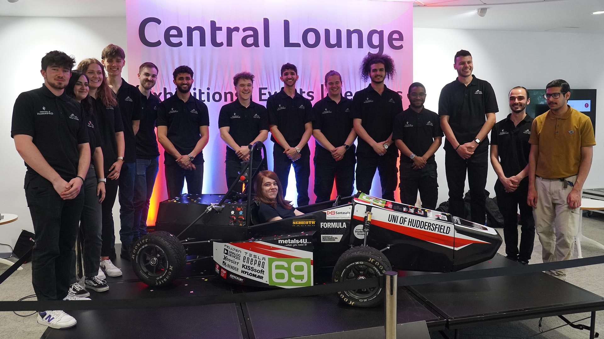 A group of students standing behind a car on a stage