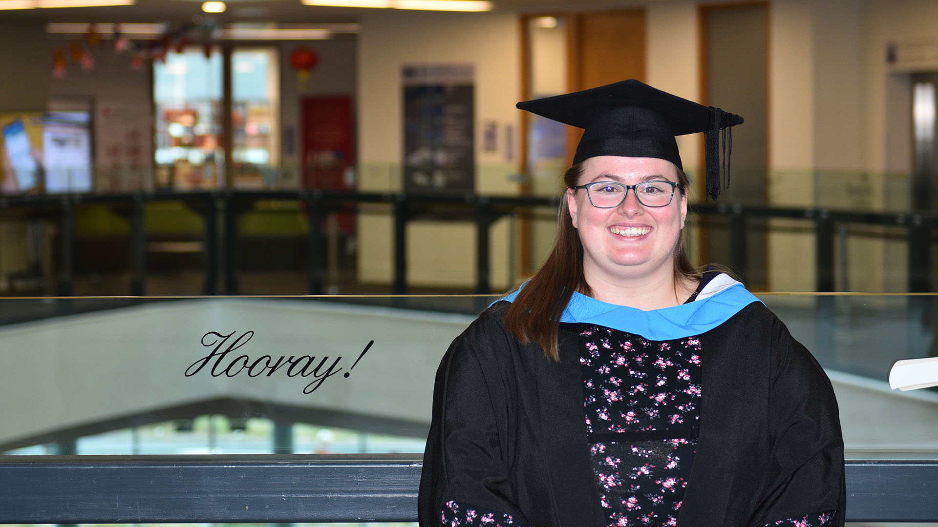 Vanessa Rodgers in her graduating gown by a sign that says hooray