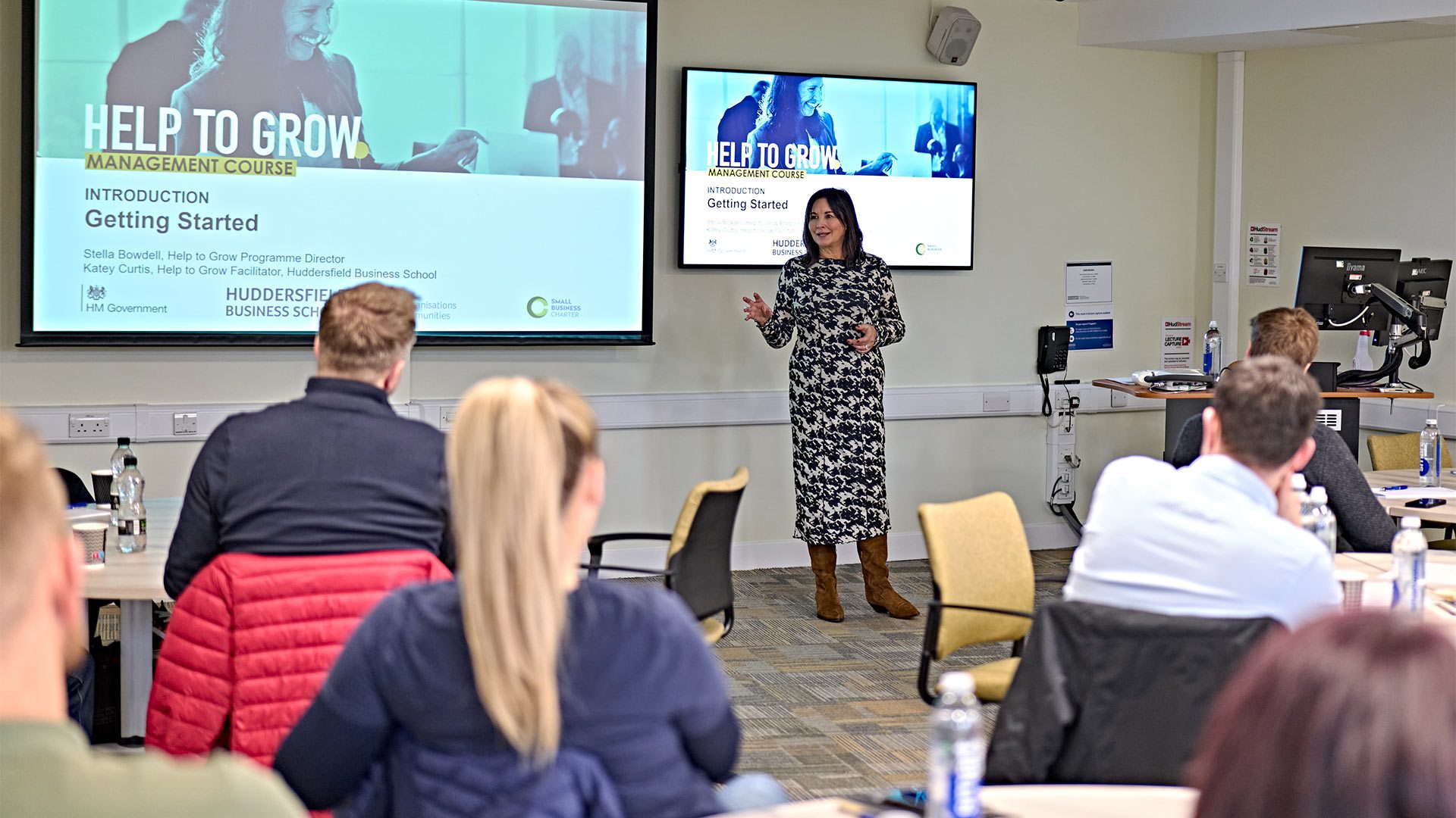 A lecturer presenting at the front of a class of students