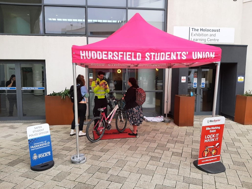 Two students talking a police officer, outside on campus.