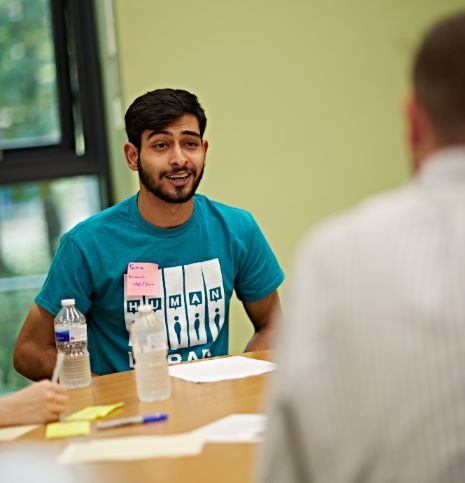 A man sat at a round table, smiling while mid-conversation