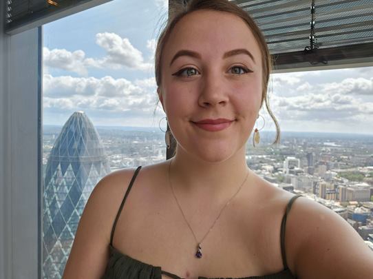 A brunette woman is smiling in front of a cityscape background